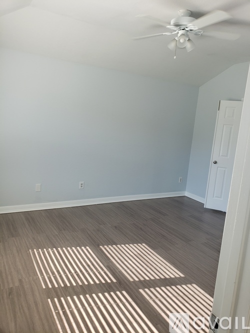 A room with a ceiling fan and light, and a wooden floor with a rug.