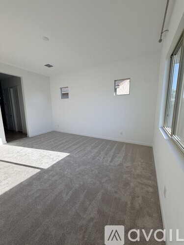 A room with a grey carpet and a window on the right side.