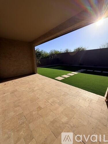 A patio with a tiled floor and a view of a green lawn and trees.