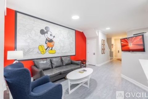 A living room with a grey couch and a Mickey Mouse mural on the wall.