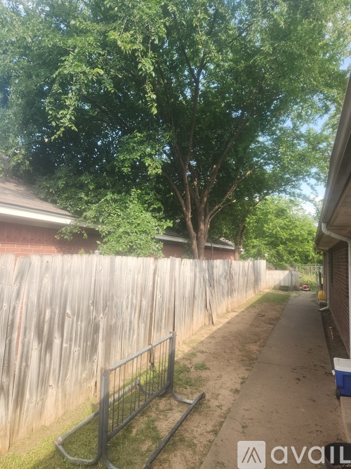 A tree-lined residential street with a sidewalk and a fence.