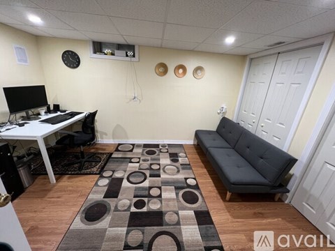 A living room with a black couch, a white desk, and a rug with circles and squares.
