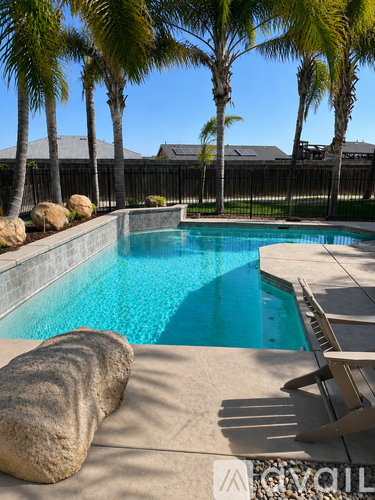 A pool surrounded by palm trees and a rock.