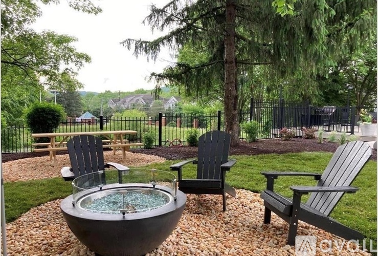 A black chair sits in a garden with a hot tub in the middle.