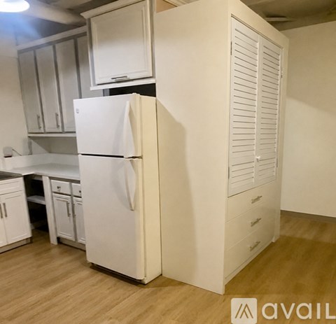 A white refrigerator in a kitchen with wooden flooring.