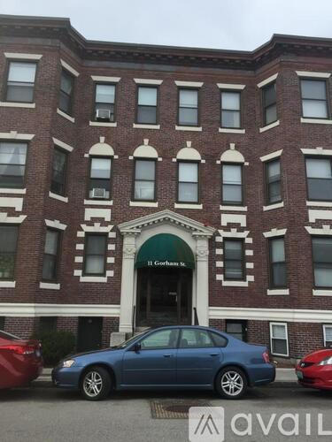 A blue car is parked in front of a brick building with a green awning.