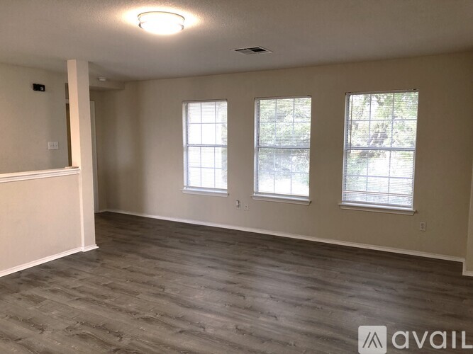 A spacious room with wooden flooring and two windows.