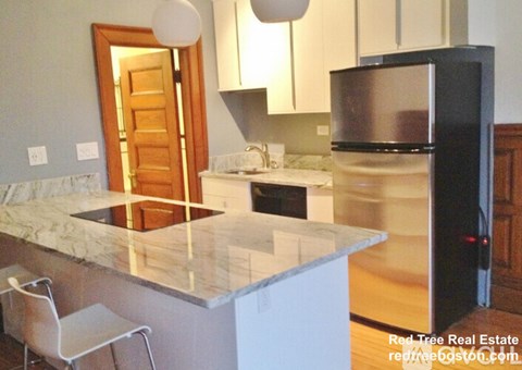 A kitchen with a marble countertop and a black refrigerator.
