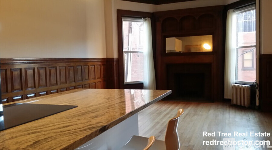 A wooden table with a bench in front of a fireplace in a room with a window.