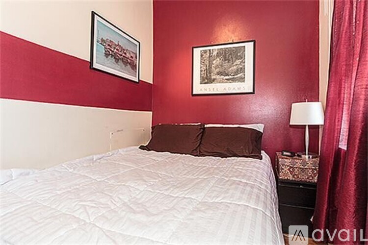 A bedroom with a white bed and two framed pictures on the wall.