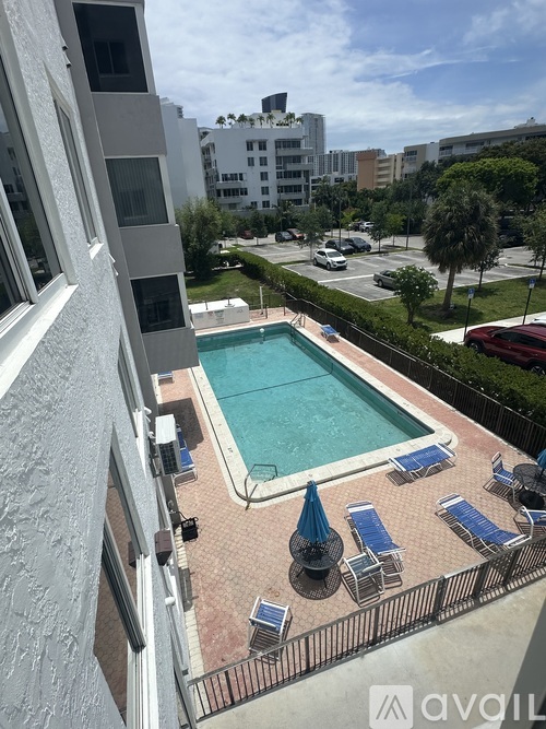 A pool surrounded by chairs and umbrellas is seen from a window.