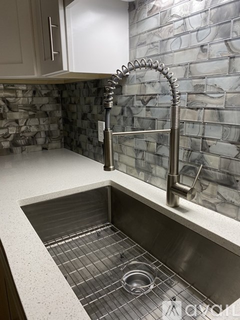 A kitchen sink with a silver faucet and a stone wall behind it.