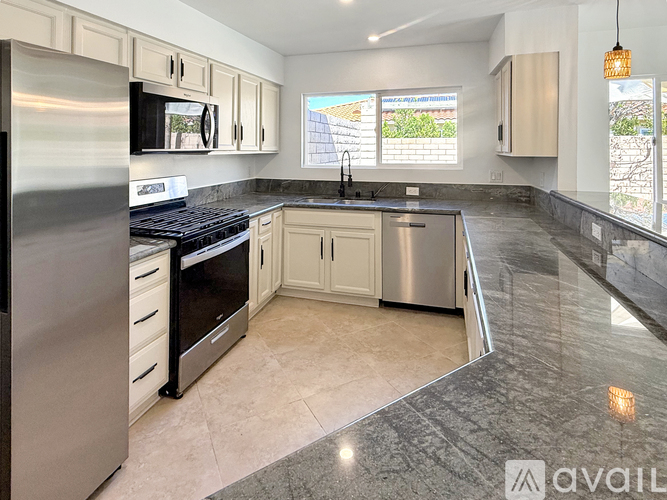 A kitchen with a black counter top and stainless steel appliances.