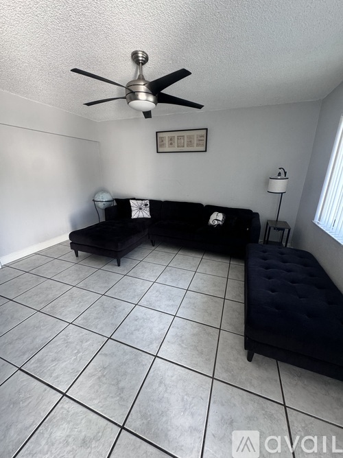A living room with a black couch and a fan on the ceiling.