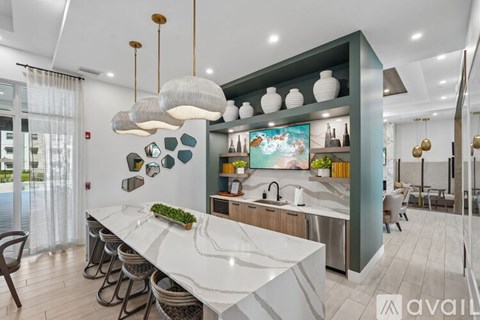 A modern kitchen with a long white island and pendant lights.