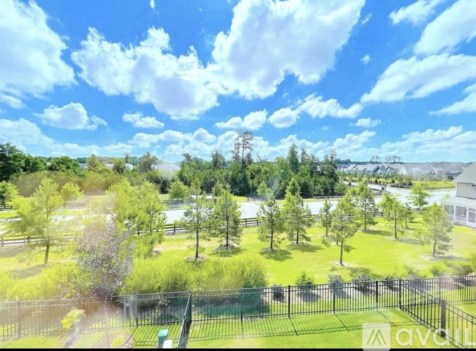 A view of a green lawn with trees and a fence in the foreground.