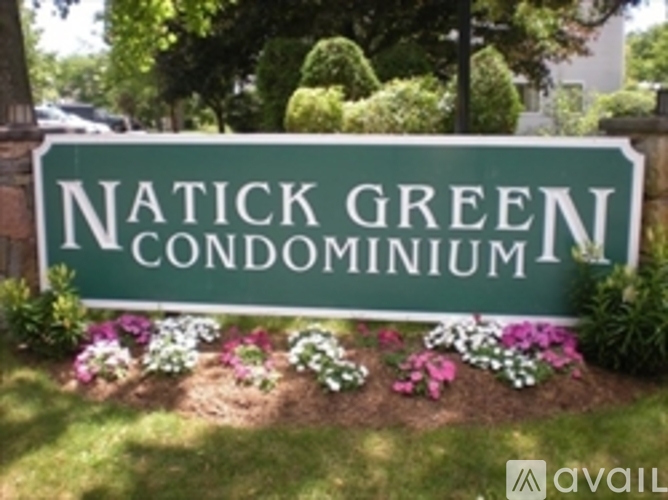 A sign for Natick Green Condominium surrounded by flowers.