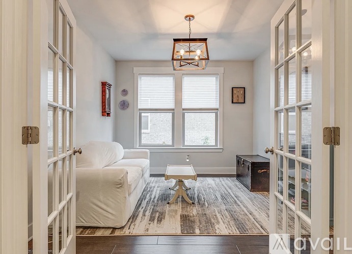 A white couch sits in a room with a wooden floor and a chandelier hanging from the ceiling.
