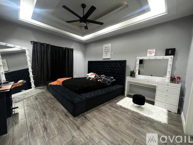 A bedroom with a black bed, a desk with a computer, and a ceiling fan.