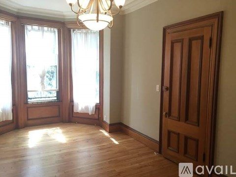A room with a wooden floor, a chandelier, and a large window with curtains.