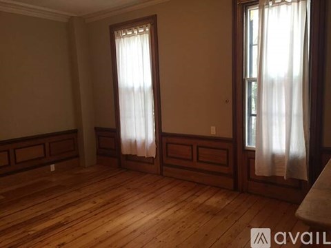 A room with wooden floors and two windows with curtains.