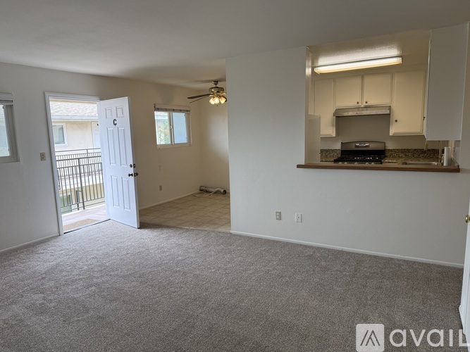 A spacious living room with a ceiling fan and a kitchenette in the background.