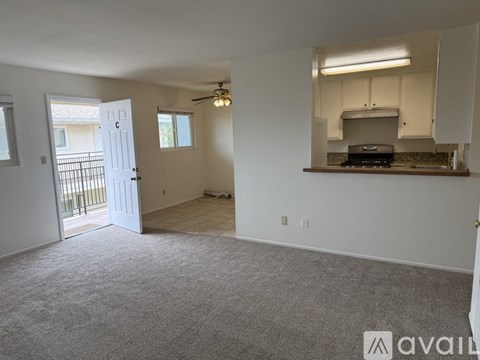 A spacious living room with a ceiling fan and a kitchenette in the background.