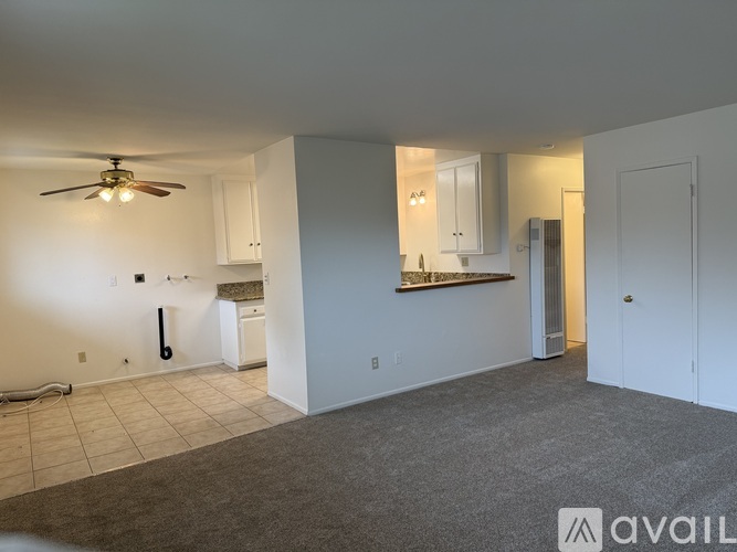 A spacious living room with a ceiling fan and a kitchen area with white cabinets.