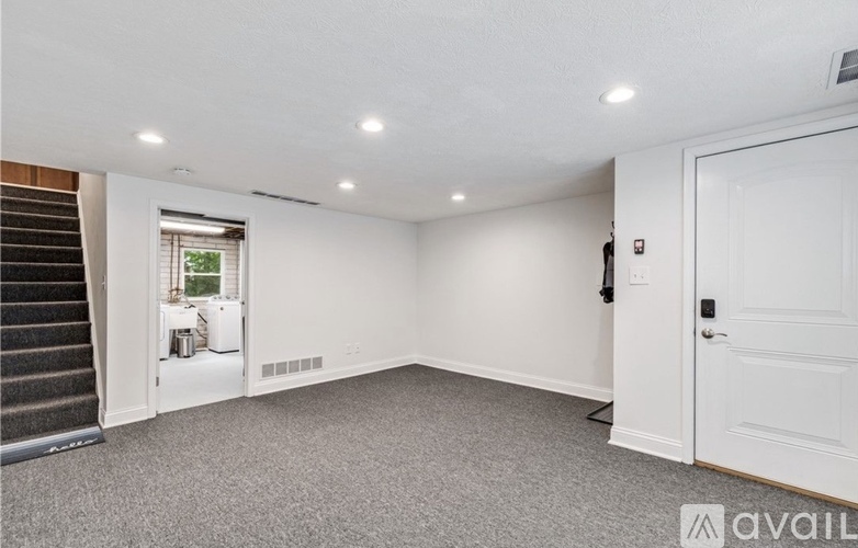 A spacious room with a staircase on the left and a door on the right.