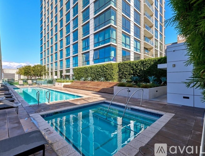 A swimming pool in front of a tall building with a hedge on the side.