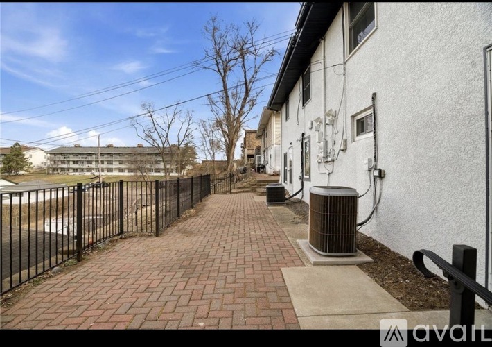 A brick pathway leads to a white building with a black fence on the left.