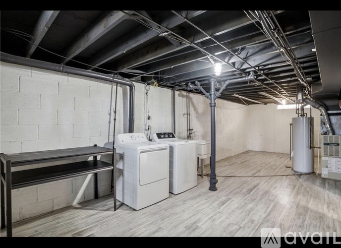 A large industrial room with a washing machine and dryer, a bench, and a pipe running along the wall.