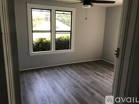 A room with a ceiling fan and a window overlooking a green area.