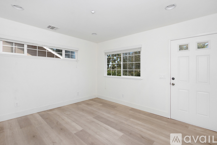 A room with white walls, a wooden floor, and a window with a view of trees.