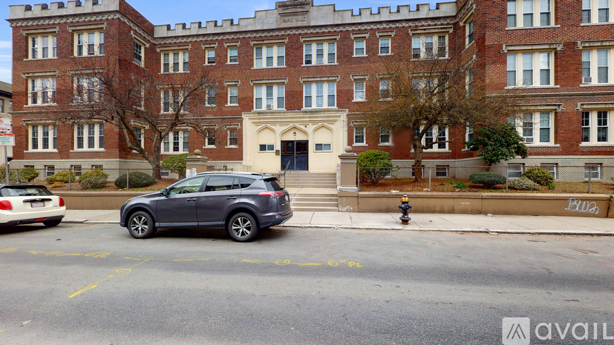 A grey car is parked in a parking lot in front of a red brick building.
