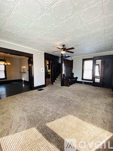A living room with a carpeted floor and a ceiling fan.