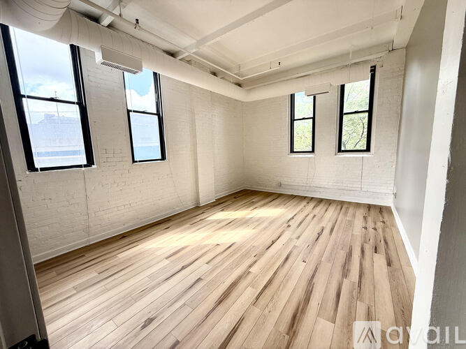 A room with wooden flooring and three windows.