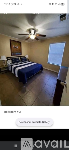 A bedroom with a bed, a ceiling fan, and a painting on the wall.