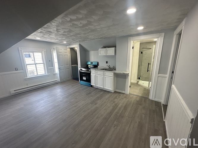 A room with a wooden floor and white walls, with a window on the left side.