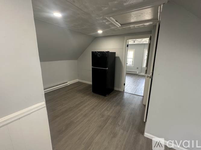 A black fridge in a room with wooden flooring and white walls.