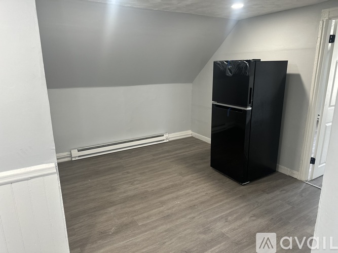 A black fridge stands in a room with wooden flooring and white walls.