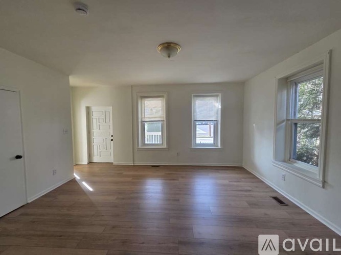A spacious room with wooden floors and three windows.