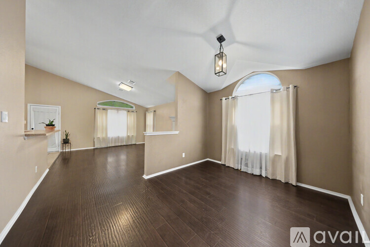 A spacious room with wooden floors and a large arched window.
