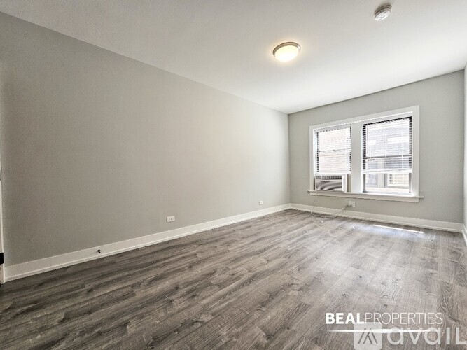 A spacious room with wooden flooring and a window with blinds.