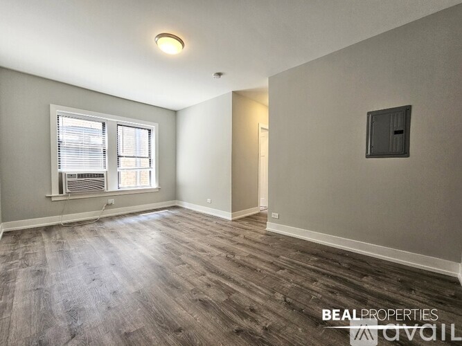 A spacious room with wooden flooring and a window with blinds.