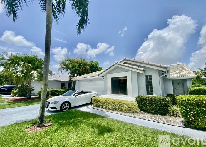 A white house with a car parked in front and a palm tree to the left.
