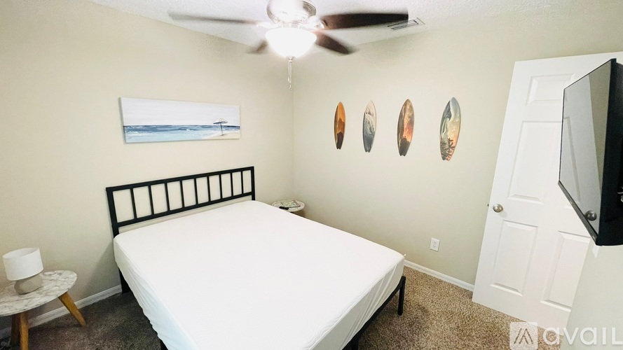 A bedroom with a bed, a ceiling fan, and a painting on the wall.