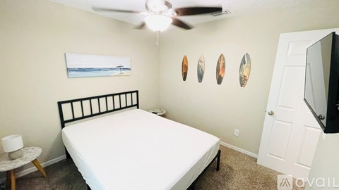 A bedroom with a bed, a ceiling fan, and a painting on the wall.