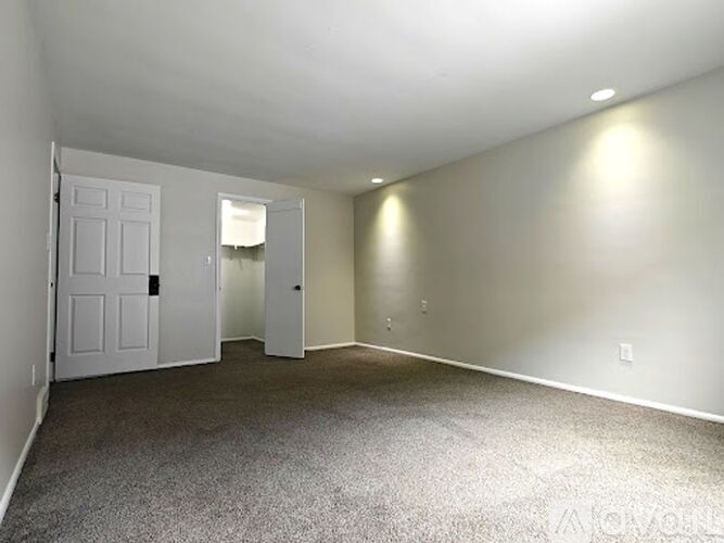 A spacious empty room with carpeted floor and white walls.