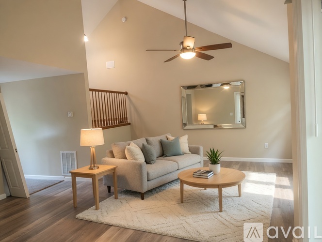 A living room with a grey couch, a wooden coffee table, a side table with a lamp, a ceiling fan, and a mirror on the wall.